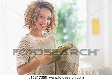 Stock Image - Young woman drying plates in kitchen. Fotosearch