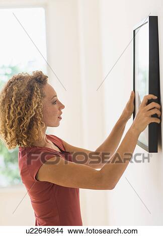 Young woman hanging print on wall View Large Photo Image Picture - Young woman hanging print on wall. Fotosearch