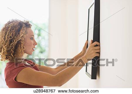 Young woman hanging print on wall View Large Photo Image Stock Photo - Young woman hanging print on wall. Fotosearch