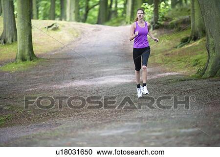Stock Image - Young woman jogging in woods. Fotosearch