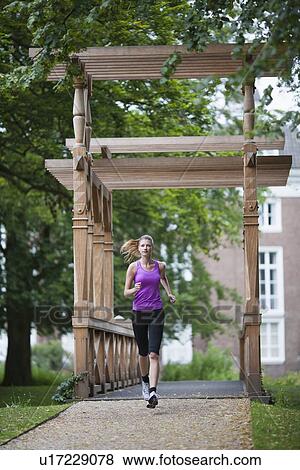 Young woman jogging over bridge in park View Large Photo Image Stock Photo - Young woman jogging over bridge in park. Fotosearch