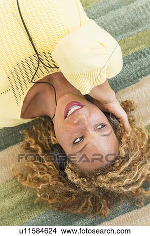 Young woman lying on carpet and listening to music on headphones View Large Photo Image Picture - Young woman lying on carpet and listening to music on headphones. Fotosearch