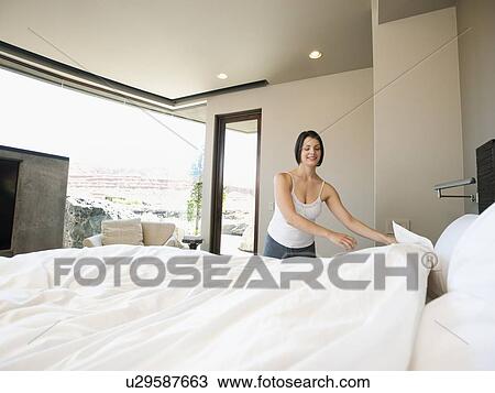 Stock Image - Young woman making bed. Fotosearch