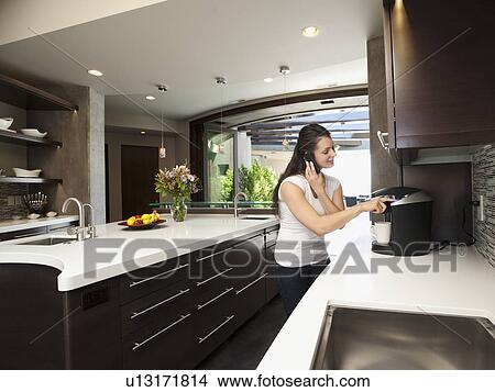 Young woman making morning coffee while using mobile phone View Large Photo Image Picture - Young woman making morning coffee while using mobile phone. Fotosearch
