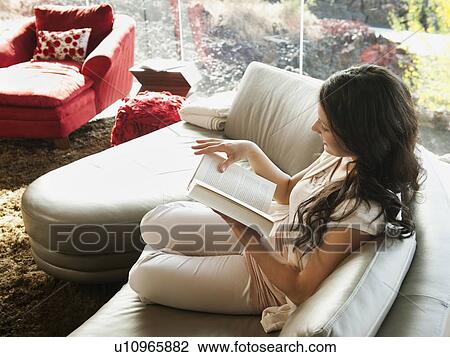Young woman reading book while sitting on sofa View Large Photo Image Stock Image - Young woman reading book while sitting on sofa. Fotosearch