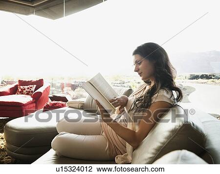 Young woman reading book while sitting on sofa View Large Photo Image Stock Image - Young woman reading book while sitting on sofa. Fotosearch