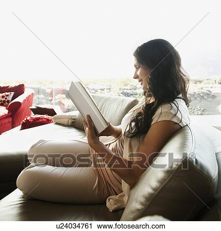 Young woman reading book while sitting on sofa View Large Photo Image Stock Image - Young woman reading book while sitting on sofa. Fotosearch