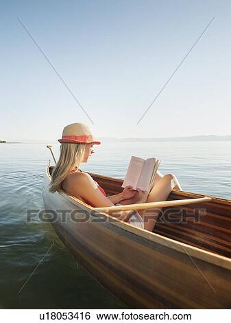 Stock Photograph - Young woman relaxing in canoe, and reading book. Fotosearch