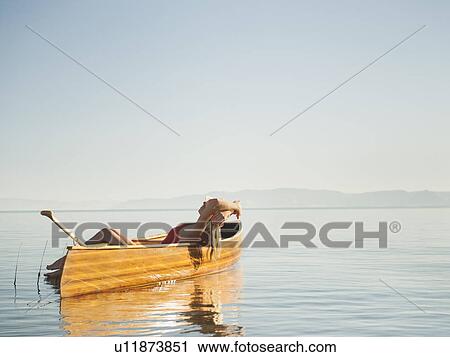 Stock Image - Young woman relaxing in canoe with arms raised. Fotosearch
