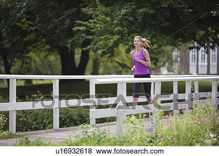 Stock Photo - Young woman running over bridge in park. Fotosearch