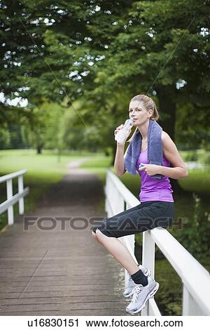 Young woman sitting on bridge after running and drinking water from bottle View Large Photo Image Stock Image - Young woman sitting on bridge after running and drinking water from bottle. Fotosearch