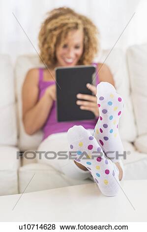 Stock Photo - Young woman sitting on sofa with digital tablet. Fotosearch