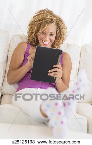 Stock Photo - Young woman sitting on sofa with digital tablet. Fotosearch