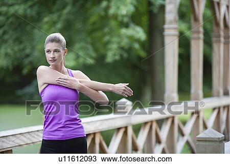 Stock Image - Young woman stretching arm on wooden bridge after running.. Fotosearch
