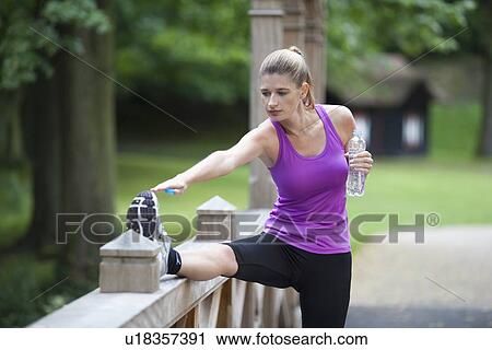 Stock Image - Young woman stretching her leg on bridge after running. Fotosearch