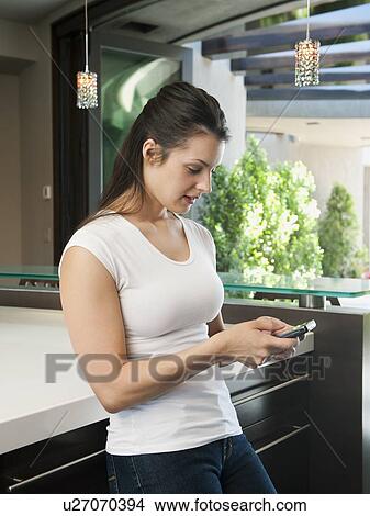 Young woman text-messaging in her kitchen View Large Photo Image Picture - Young woman text-messaging in her kitchen. Fotosearch