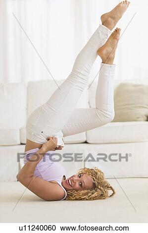 Stock Image - Young woman trying on tight jeans on the floor. Fotosearch