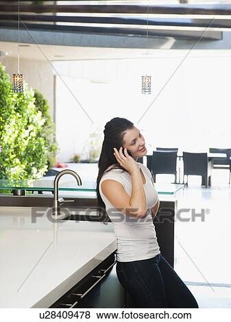 Young woman using mobile phone in her kitchen View Large Photo Image Stock Photo - Young woman using mobile phone in her kitchen. Fotosearch