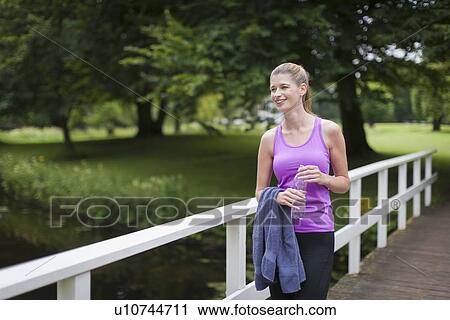 Young woman walking on bridge after running and holding towel and bottle of water View Large Photo Image Stock Image - Young woman walking on bridge after running and holding towel and bottle of water. Fotosearch
