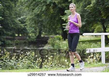 Young woman walking over bridge with bottle of water in her hand View Large Photo Image Stock Photo - Young woman walking over bridge with bottle of water in her hand. Fotosearch
