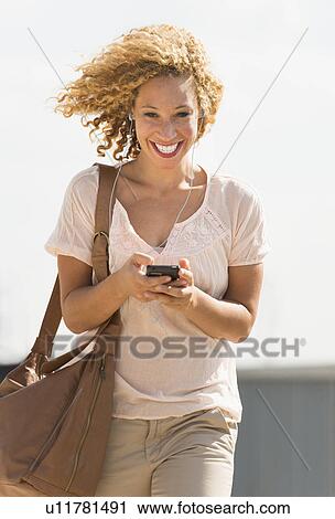 Stock Image - Young woman walking with headphones. Fotosearch