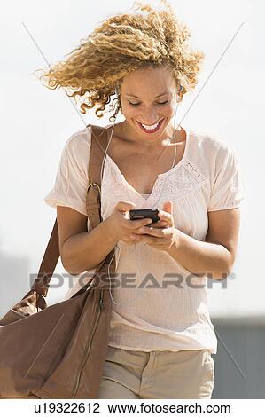 Stock Image - Young woman walking with headphones. Fotosearch