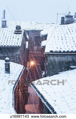 Stock Image - Aerial view of medieval street - stone houses and tiled roofs, covered with snow in early dawn light, MonteCastello di Vibio, Umbria, Italy. Fotosearch