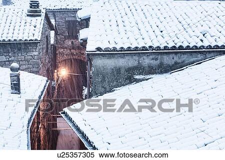 Stock Photography - Aerial view of medieval street - stone houses and tiled roofs, covered with snow in early dawn light, MonteCastello di Vibio, Umbria, Italy. Fotosearch