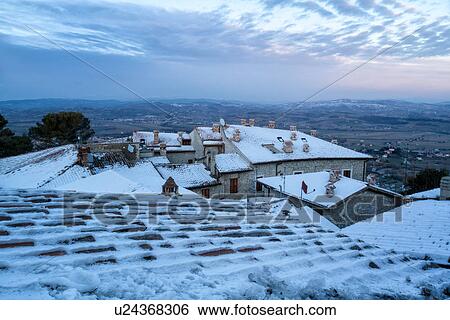 Stock Photograph - Aerial view of medieval town - stone houses and tiled roofs, covered with snow in early dawn light, overlooking Tiber Valley and distant hills, sunrise, MonteCastello di Vibio, Umbria, Italy. Fotosearch