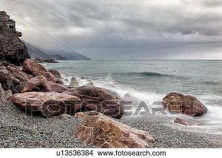 Picture - Beach and coastline at Monterosso al Mare: pink rocks at sea edge with motion blur of waves and stormy sky, Cinque Terre. Liguria, Italy. Fotosearch