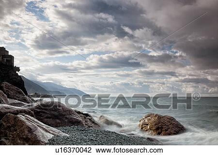 Beach and coastline at Monterosso al Mare: pink rocks at sea edge with motion blur of waves, single house perched above, and stormy sunset sky, Cinque Terre. Liguria, Italy View Large Photo Image Stock Image - Beach and coastline at Monterosso al Mare: pink rocks at sea edge with motion blur of waves, single house perched above, and stormy sunset sky, Cinque Terre. Liguria, Italy. Fotosearch