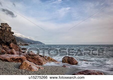 Stock Photograph - Beach and coastline at Monterosso al Mare: pink rocks at sea edge with motion blur of waves and stormy sky, Cinque Terre. Liguria, Italy. Fotosearch
