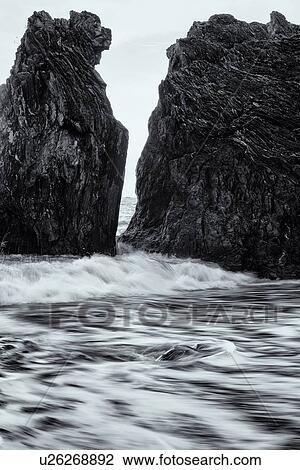 Stock Image - Beach at Monterosso al Mare: imposing black rock at sea edge with motion blur of waves, grey sky, single boat beyond, Cinque Terre. Liguria, Italy. Fotosearch