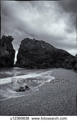 Beach at Monterosso al Mare: imposing black rock at sea edge with motion blur of waves, grey sky, small rocks in foreground, monochrome, Cinque Terre. Liguria, Italy View Large Photo Image Stock Photo - Beach at Monterosso al Mare: imposing black rock at sea edge with motion blur of waves, grey sky, small rocks in foreground, monochrome, Cinque Terre. Liguria, Italy. Fotosearch