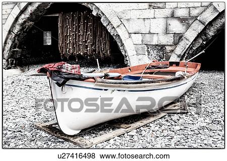 Stock Photo - Beach of San Fruttuoso, with view of fishing boat on beach with abbey arches and fishing nets hanging beyond, destaurated image, Camogli, Liguria, Italy. Fotosearch