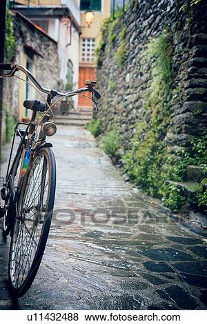 Bicycle close up parked on path, with mossy wall and houses in background, rainy day, Monterosso al Mare, Cinque Terre, Liguria, Italy View Large Photo Image Stock Photo - Bicycle close up parked on path, with mossy wall and houses in background, rainy day, Monterosso al Mare, Cinque Terre, Liguria, Italy. Fotosearch