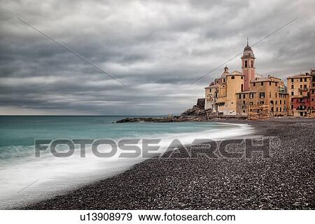 Stock Photo - Camogli: beach and sea with waves motion blur, church tower and surrounding buildings beyond, grey sky with dramatic clouds, Liguria, Italy. Fotosearch