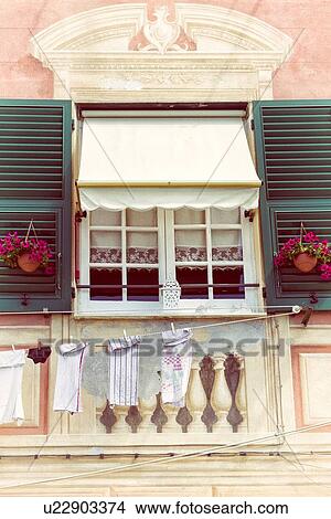Picture - Camogli: facade of apartment window, with lace curtains, green wooden shutters, red flowers, building details frecoed onto stucco, laundry hanging, Liguria, Italy. Fotosearch