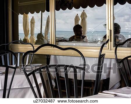 Camogli: reflection in restaurant window of customers seated at tables,, with umbrellas and sea beyond, with attractive chairs in foreground, Liguria, Italy View Large Photo Image Stock Photo - Camogli: reflection in restaurant window of customers seated at tables,, with umbrellas and sea beyond, with attractive chairs in foreground, Liguria, Italy. Fotosearch