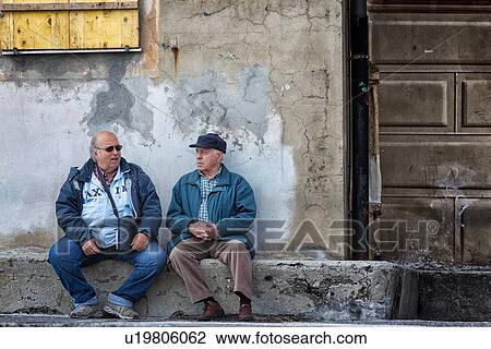 Camogli: two men sitting on stone wall chatting with old cracked stucco wall behind and yellow wooden window shutter above, Liguria, Italy View Large Photo Image Stock Image - Camogli: two men sitting on stone wall chatting with old cracked stucco wall behind and yellow wooden window shutter above, Liguria, Italy. Fotosearch