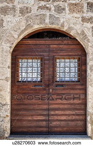 Cività di Bagnoregio: close up view of arched doorway with double wooden doors, each with window covered by white lace curtain and metal grate, surrounded by stone wall, Umbria, Italy View Large Photo Image Stock Image - Cività di Bagnoregio: close up view of arched doorway with double wooden doors, each with window covered by white lace curtain and metal grate, surrounded by stone wall, Umbria, Italy. Fotosearch