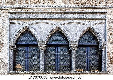 Cività di Bagnoregio: detail of Romanesque-Gothic lead glass window with three arched sections divided by decorated stone columns, and carved frieze of family crests above, Umbria, Italy View Large Photo Image Stock Photo - Cività di Bagnoregio: detail of Romanesque-Gothic lead glass window with three arched sections divided by decorated stone columns, and carved frieze of family crests above, Umbria, Italy. Fotosearch