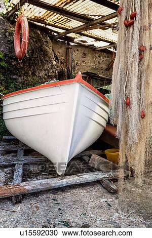 Stock Image - Close up of fishing boat in storage area with nets and life ring hanging from corrugated plastic, light streaming through, Camogli, Liguria, Italy. Fotosearch