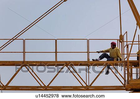 Stock Photo - Close up of horizontal part of yellow crane near cabin with man in yellow jacket, and red safety helmet sitting, Umbria, Italy. Fotosearch