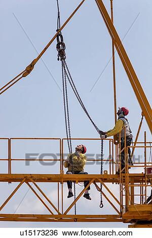 Close up of horizontal part of yellow crane near cabin with two men in yellow jackets, and red safety helmets, working with hanging chains and hooks, Umbria, Italy View Large Photo Image Stock Photograph - Close up of horizontal part of yellow crane near cabin with two men in yellow jackets, and red safety helmets, working with hanging chains and hooks, Umbria, Italy. Fotosearch