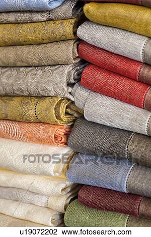 Stock Image - Close up view of display of linen and cotton tablecloths woven on Jacquard loom, 2 piles on shelf, Umbria, Italy. Fotosearch