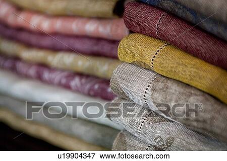 Stock Photo - Close up view of display of linen and cotton tablecloths woven on Jacquard loom, 2 piles on shelf, Umbria, Italy. Fotosearch