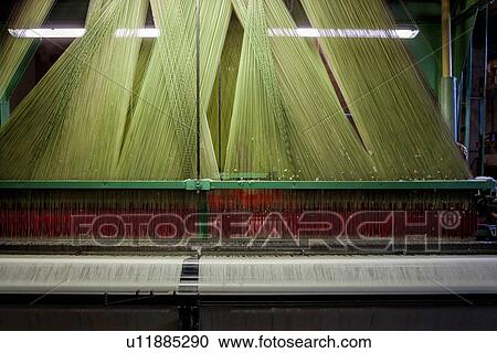 Stock Image - Close up view of Jacquard loom with pattern formed by green and red linen and cotton threads attached to heddle, fabric emerging below, Umbria, Italy. Fotosearch
