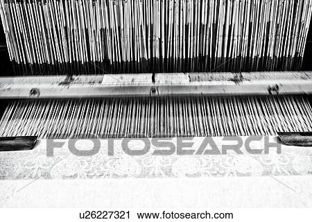 Stock Image - Close up view of Jacquard loom with pattern formed by linen and cotton threads attached to heddle, and fabric emerging below, high key monochrome image, Umbria, Italy. Fotosearch