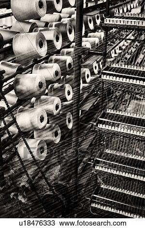 Stock Image - Close up view of spools of linen and cotton threads on racks with pattern formed by threads, high key monochrome image, Umbria, Italy. Fotosearch